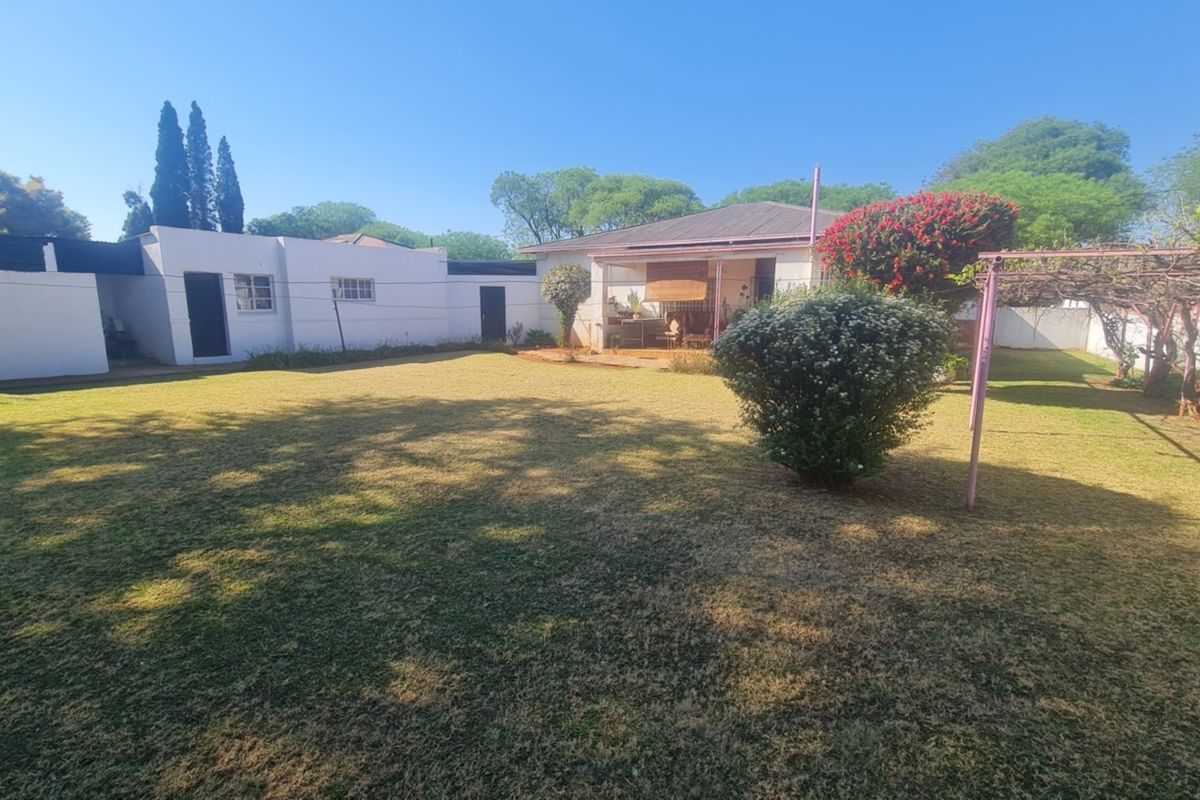 Spacious rear garden featuring a large lawn, a metal pergola structure, and a covered patio area attached to the main house.