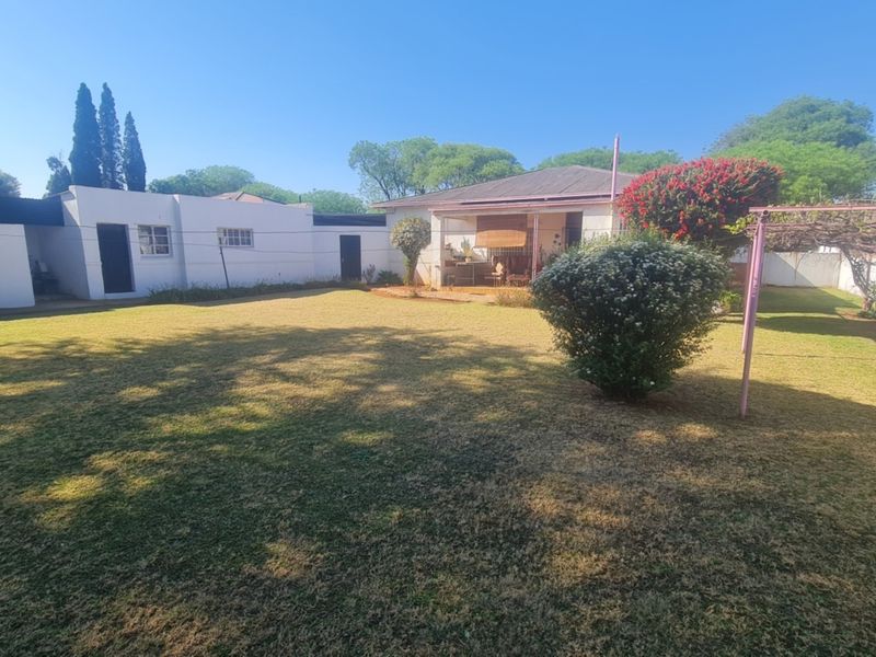 Spacious rear garden featuring a large lawn, a metal pergola structure, and a covered patio area attached to the main house.
