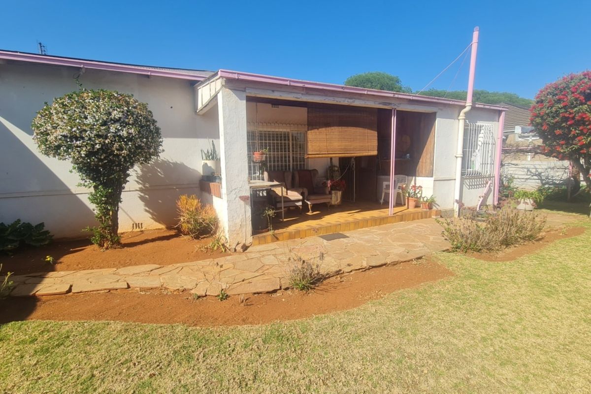 Rear view of the property featuring a covered patio area with tiled flooring, accessible from the garden with a stone pathway.