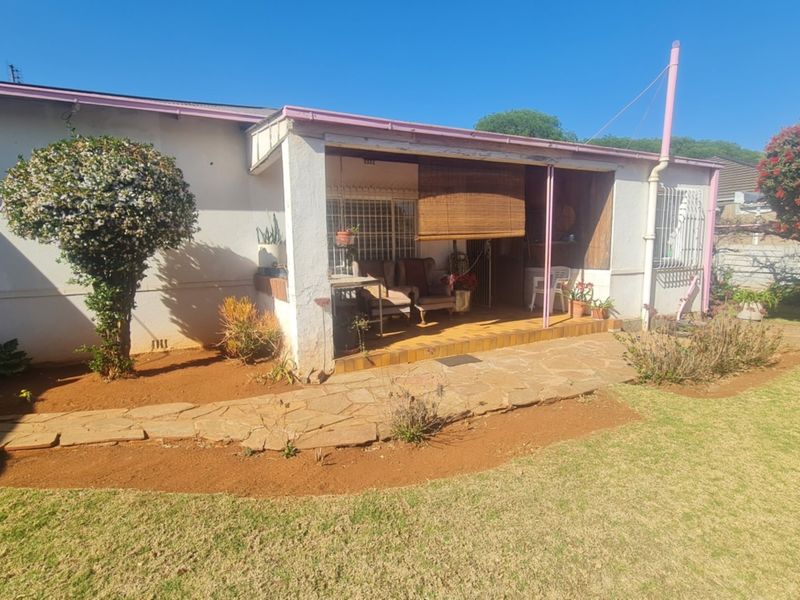 Rear view of the property featuring a covered patio area with tiled flooring, accessible from the garden with a stone pathway.