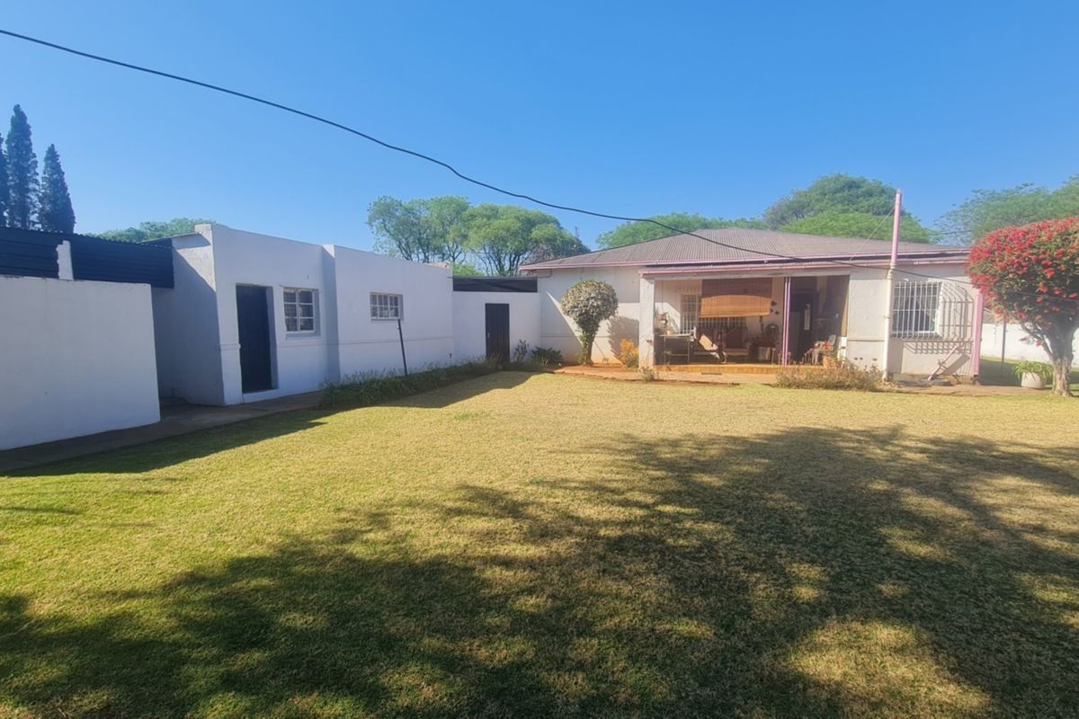 A spacious rear garden featuring a well-maintained lawn, a covered patio area, and secure boundary walls.