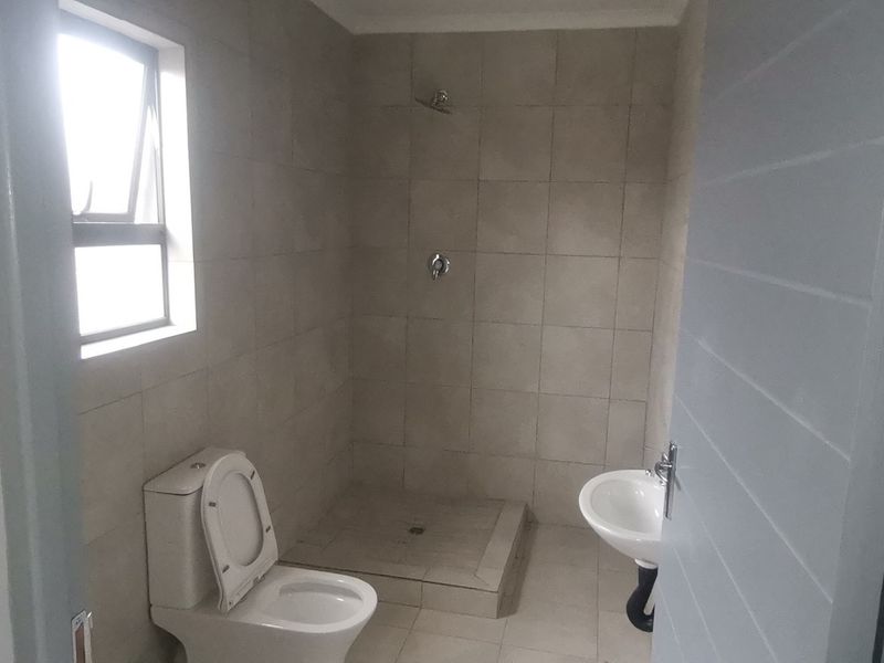 A functional bathroom featuring a walk-in shower, pedestal basin, and toilet with neutral wall and floor tiling.