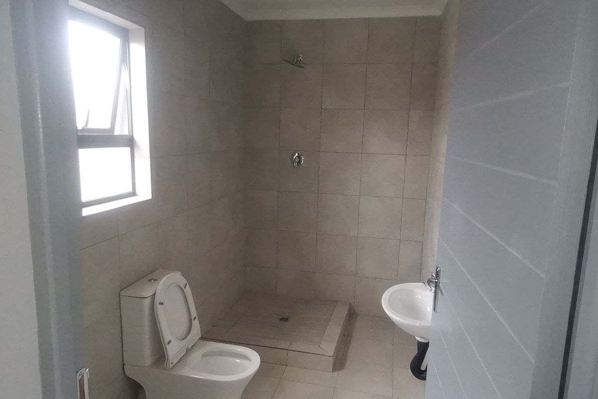 A functional bathroom featuring a walk-in shower, pedestal basin, and toilet with neutral wall and floor tiling.