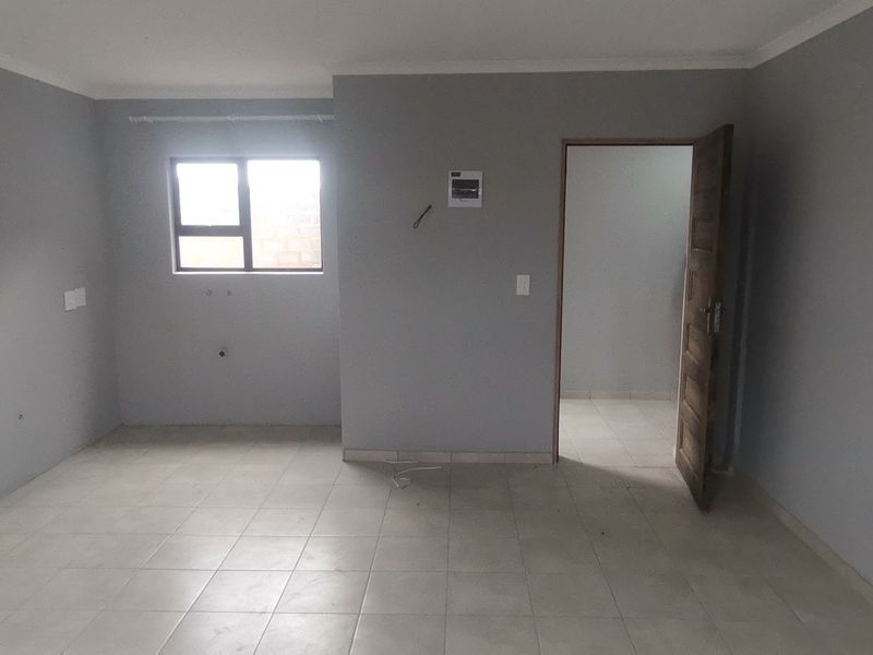 An empty, neutrally painted living area featuring tiled flooring, an aluminium window, and an internal doorway leading to an adjacent room.