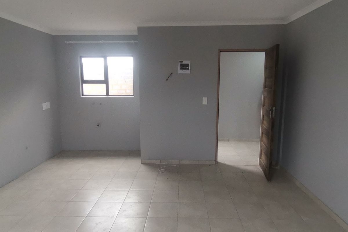 An empty, neutrally painted living area featuring tiled flooring, an aluminium window, and an internal doorway leading to an adjacent room.