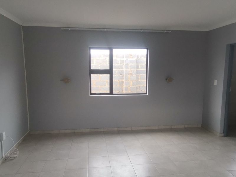 A clean, empty bedroom featuring neutral grey walls, tiled flooring, and an aluminium-framed window, providing a blank canvas for personalization.