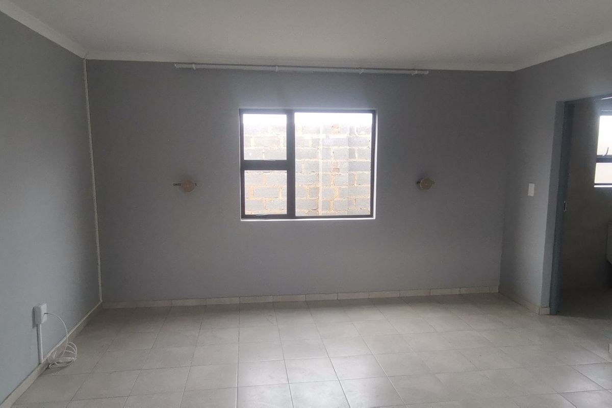 A clean, empty bedroom featuring neutral grey walls, tiled flooring, and an aluminium-framed window, providing a blank canvas for personalization.