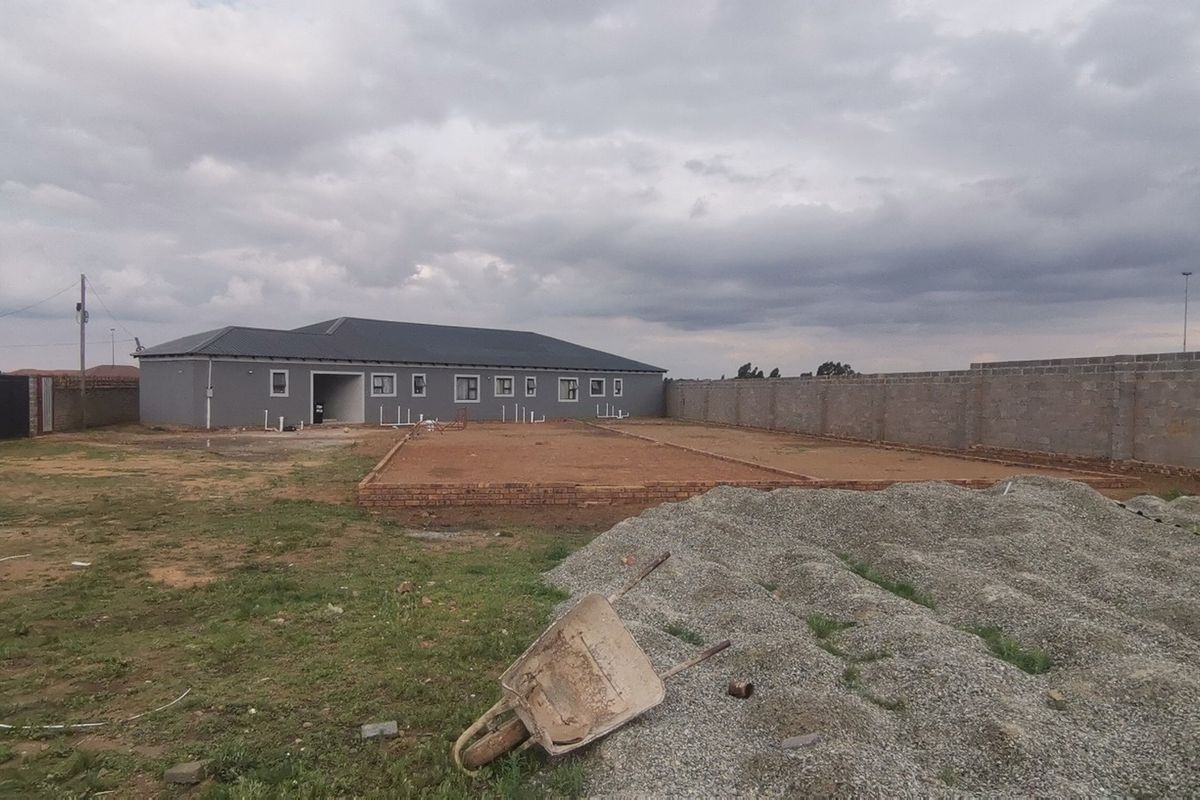 A rear view of a property under construction, featuring a large yard, perimeter wall, and a concrete foundation slab ready for further development.