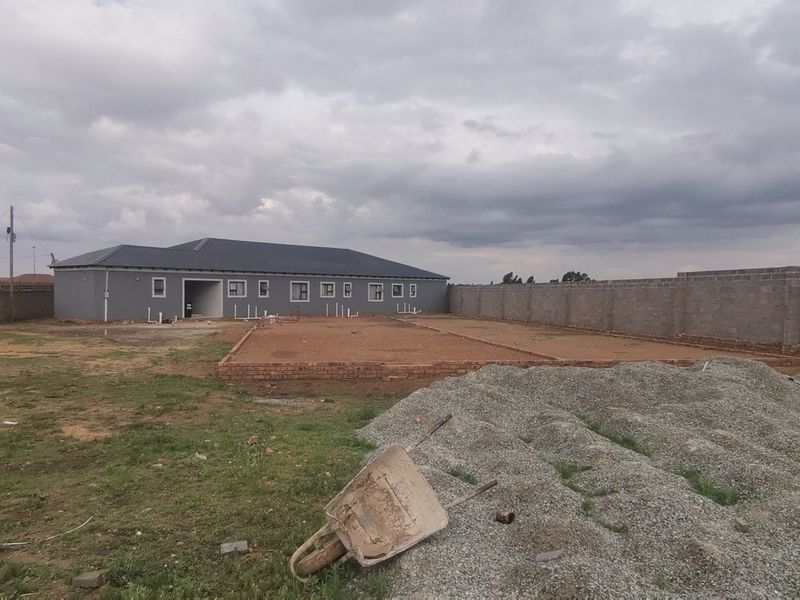 A rear view of a property under construction, featuring a large yard, perimeter wall, and a concrete foundation slab ready for further development.