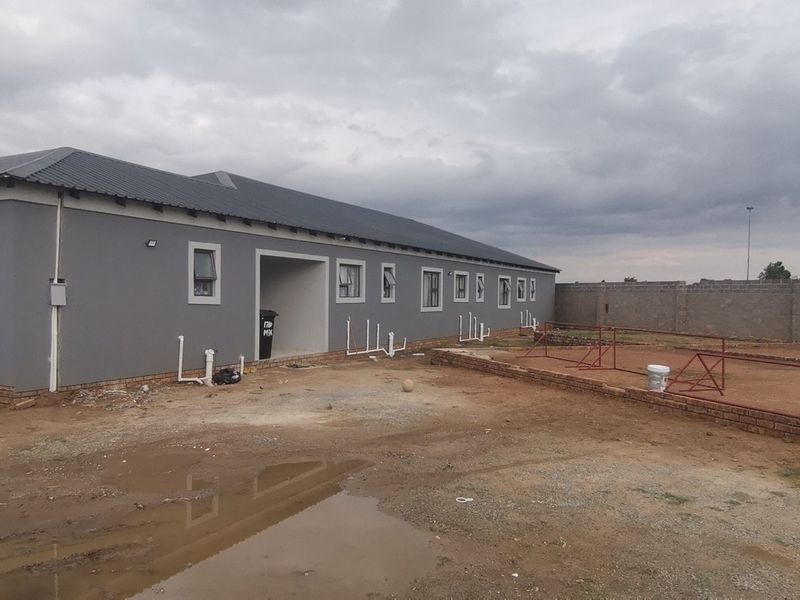 Rear view of a newly constructed house featuring a grey facade, metal roof, and unfinished exterior grounds with exposed plumbing connections.