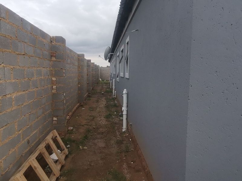 Side passage of the property featuring a plastered exterior wall, casement windows, and a concrete block boundary wall with unfinished ground.