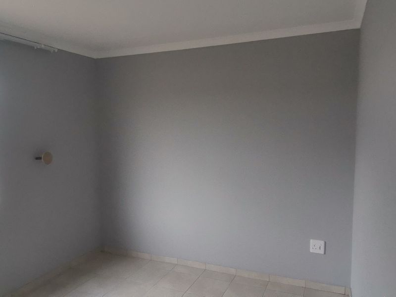 A clean, empty bedroom featuring neutral grey walls, tiled flooring, and a window with a curtain track installed.