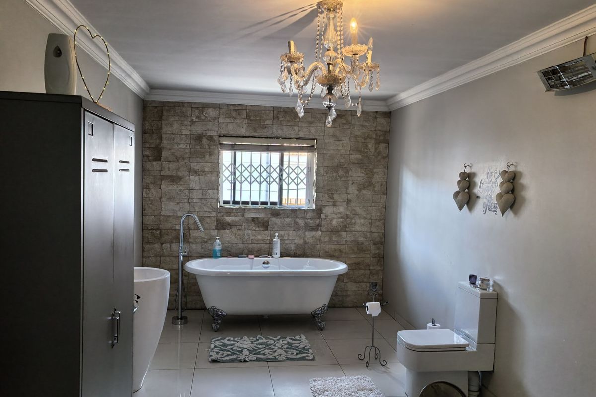 Spacious bathroom featuring a freestanding clawfoot bathtub, stone-clad feature wall, and modern toilet, complemented by elegant crown molding and tiled flooring.