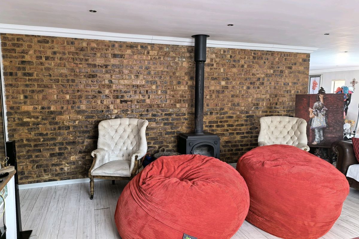 Living room featuring a prominent exposed brick wall and a central freestanding wood-burning fireplace, complemented by light-toned laminate flooring and recessed lighting.