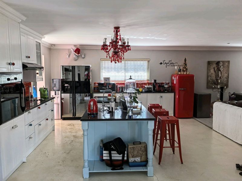 Spacious open-plan kitchen featuring a central island, white cabinetry, stone countertops, and a tiled backsplash, seamlessly connecting to the living area.