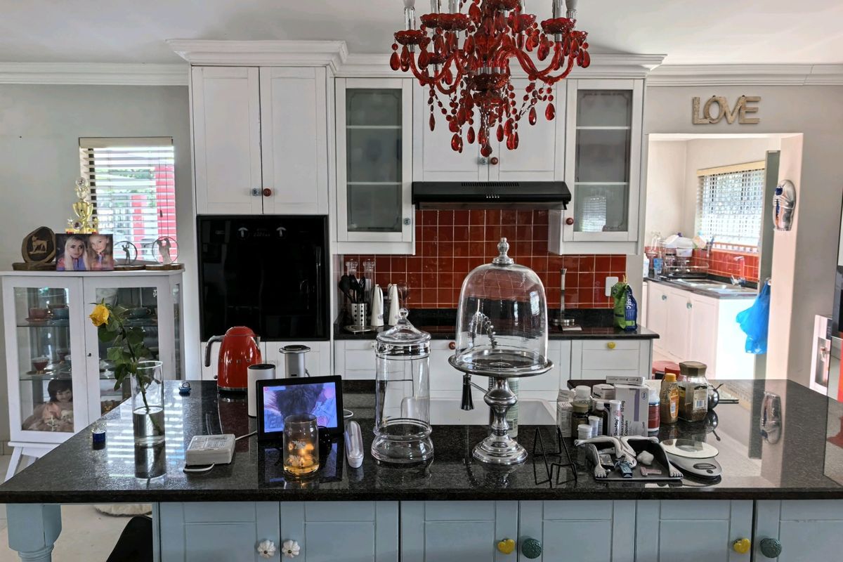 A kitchen featuring a central island with granite countertops, built-in oven, extractor fan, and tiled backsplash, with an adjacent scullery area visible.