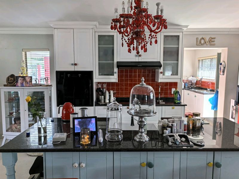 A kitchen featuring a central island with granite countertops, built-in oven, extractor fan, and tiled backsplash, with an adjacent scullery area visible.