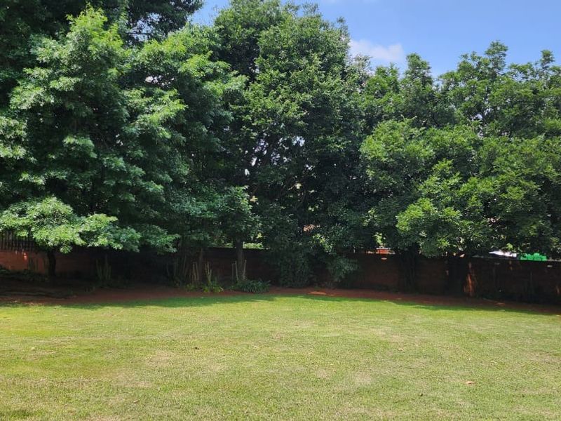 A spacious, well-maintained private garden featuring a large lawn, mature trees, and a secure brick boundary wall.