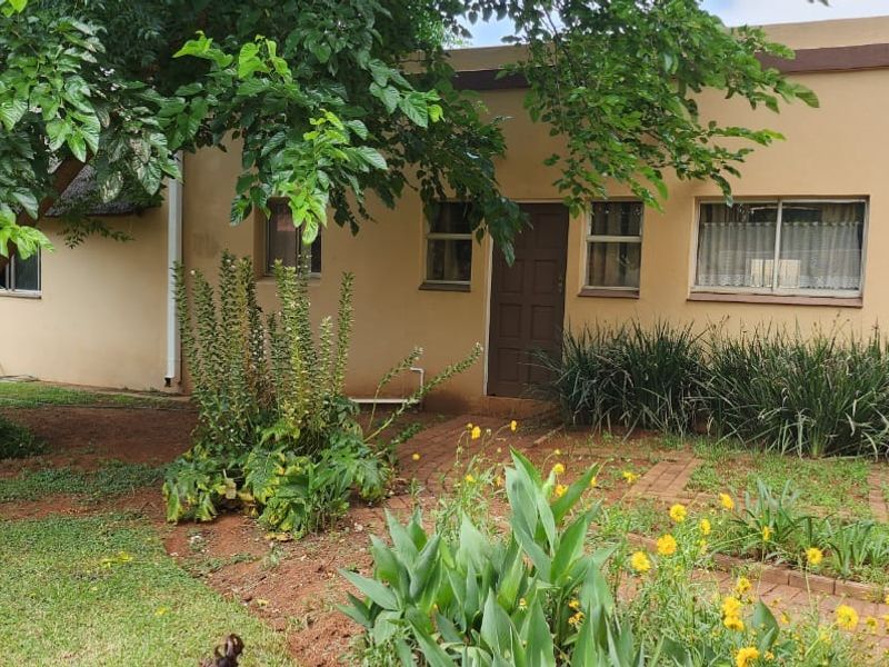 Rear view of the property featuring a landscaped garden, mature trees, and brick paved pathways leading to the building entrance.