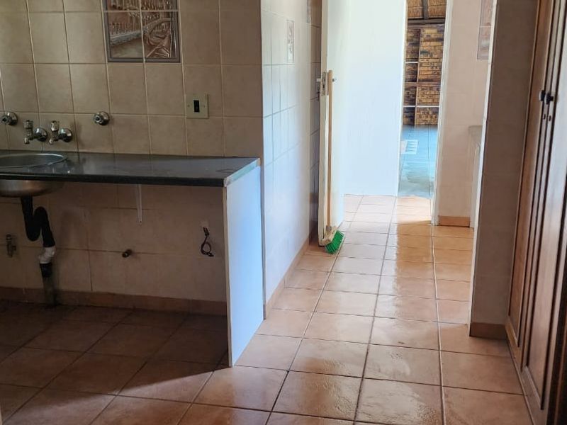 A functional laundry area featuring tiled flooring, a wall-mounted basin, and built-in cabinetry with exposed plumbing connections.