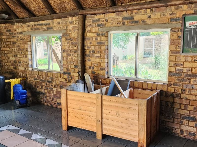 Covered outdoor patio area featuring exposed brick walls, a thatched roof, tiled flooring, and a built-in braai, overlooking the garden.
