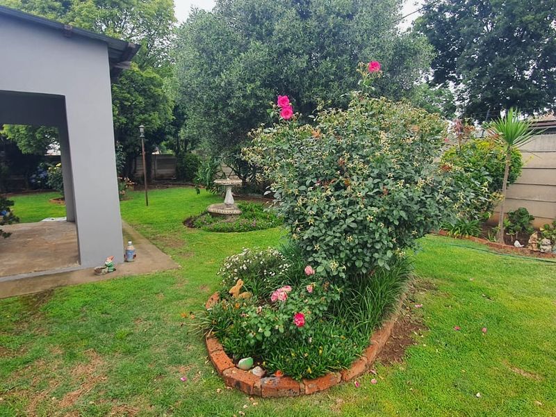A well-maintained rear garden featuring a covered patio area, lush lawn, established rose bushes, and secure precast concrete boundary walling.