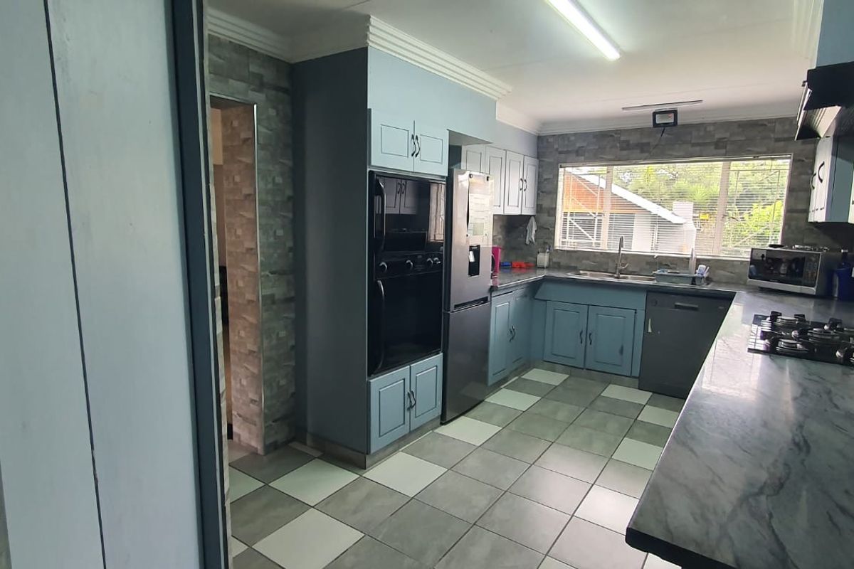 A functional kitchen featuring blue cabinetry, stone-look countertops, a built-in oven, gas hob, and tiled flooring with a view to the exterior.