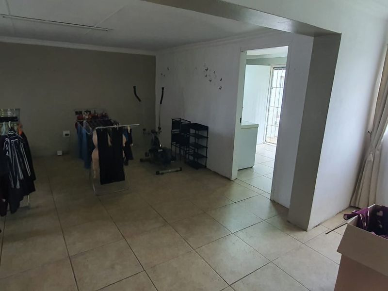 A spacious living area featuring neutral tiled flooring and coved ceilings, with an open transition to an adjacent utility space.