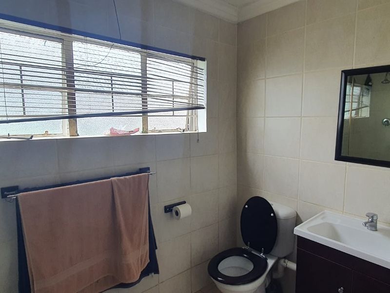 A functional bathroom featuring tiled walls, a vanity basin, and a toilet, with a window providing natural light.