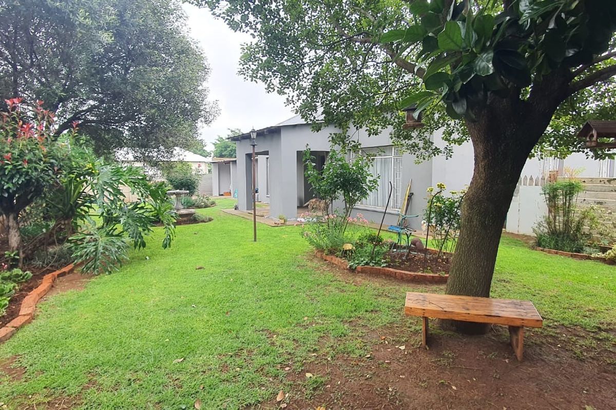 A well-maintained rear garden featuring a lush lawn, mature trees, and concrete boundary walls, providing a private outdoor space.