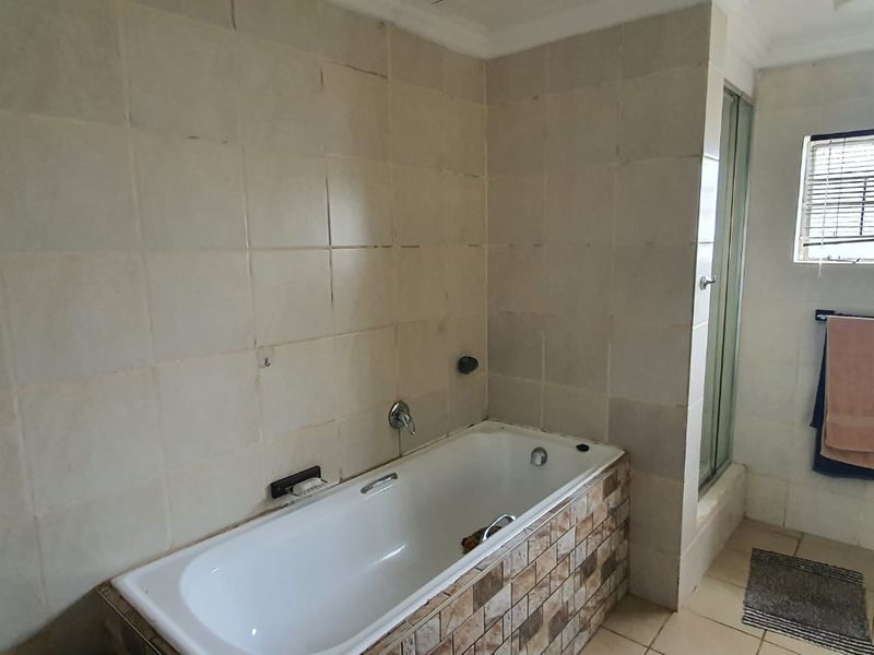 A functional bathroom featuring a built-in bathtub with decorative tiling, a separate shower enclosure, and neutral wall tiles.