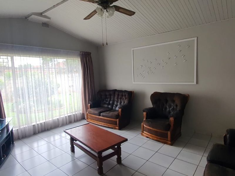 A spacious living room featuring tiled flooring, a vaulted ceiling with a fan, and a large window providing natural light.