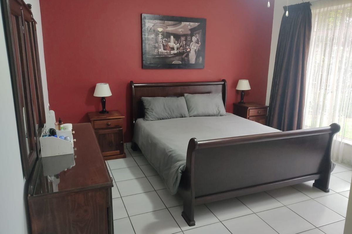 A bedroom featuring tiled flooring and a bold red accent wall, providing a functional space with natural light from the window.