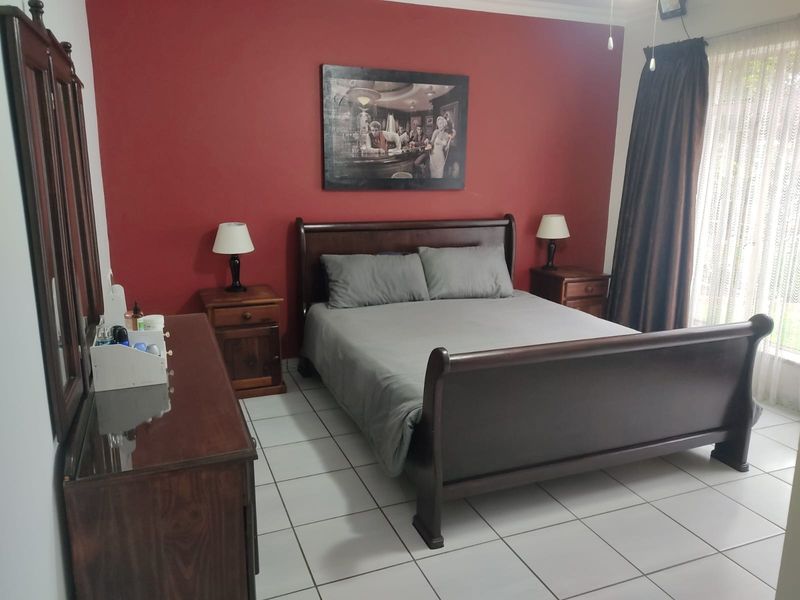 A bedroom featuring tiled flooring and a bold red accent wall, providing a functional space with natural light from the window.