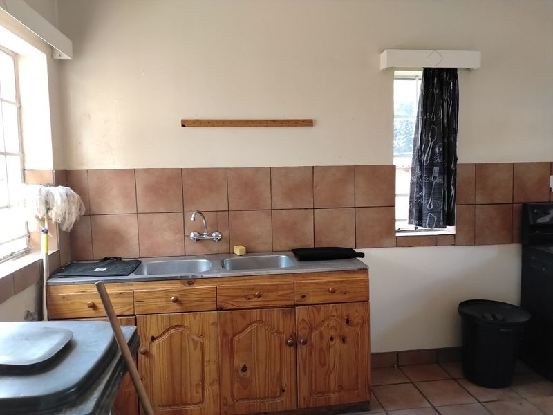 A functional kitchen area featuring wooden cabinetry, a double basin stainless steel sink, and tiled splashbacks, offering potential for modernization.