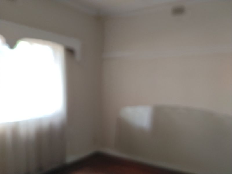 An empty bedroom featuring timber flooring, a decorative window pelmet, and a picture rail.