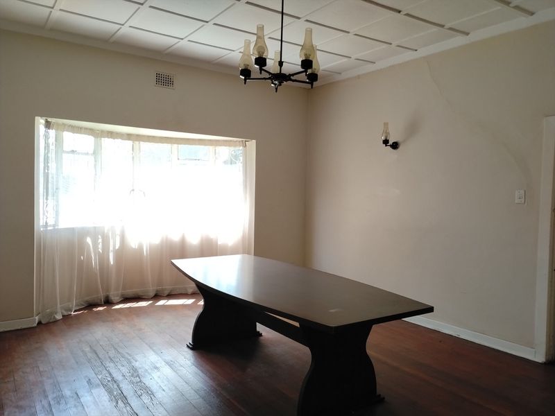 A dining room featuring original hardwood flooring, a bay window, and a classic chandelier, requiring some cosmetic attention to the walls.