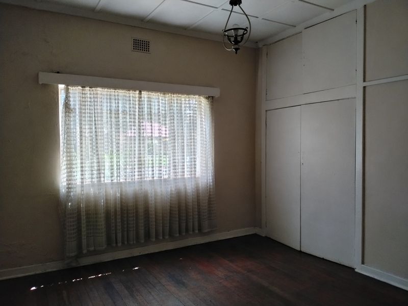An empty bedroom featuring original timber flooring, built-in storage cupboards, and a ceiling vent, offering a blank canvas for renovation.
