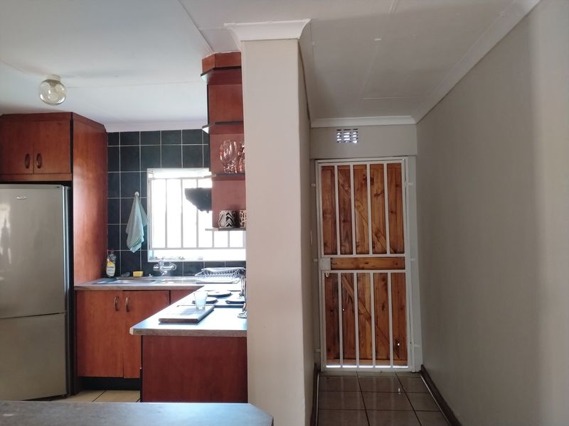 A functional kitchen featuring wooden cabinetry, tiled backsplash, and a secure wooden door with a metal security gate leading to the exterior.