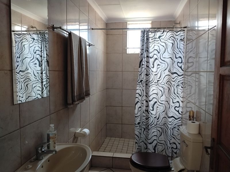 A functional bathroom featuring a shower with curtain, a standard toilet, and a wall-mounted washbasin with tiled finishes throughout.