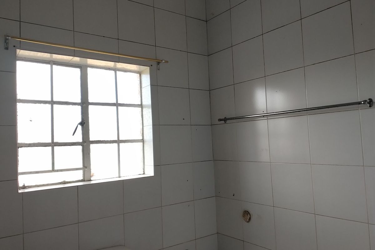 A functional bathroom space featuring white wall tiles, a window, and fixed hardware, currently in need of cosmetic updates and maintenance.
