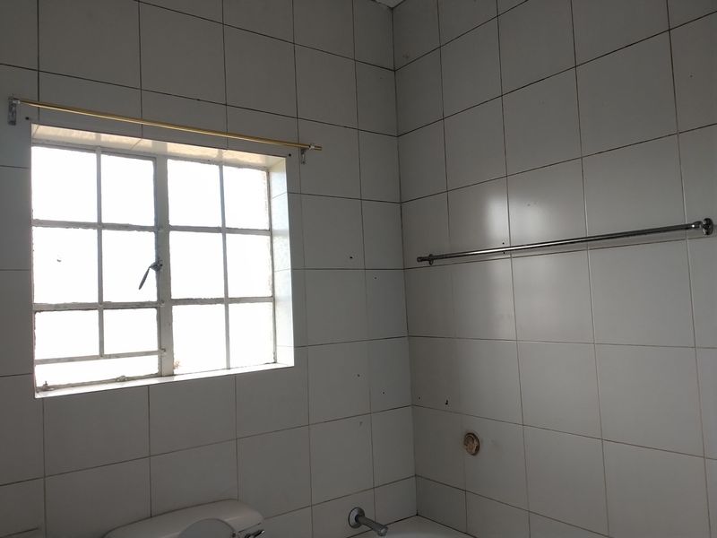A functional bathroom space featuring white wall tiles, a window, and fixed hardware, currently in need of cosmetic updates and maintenance.