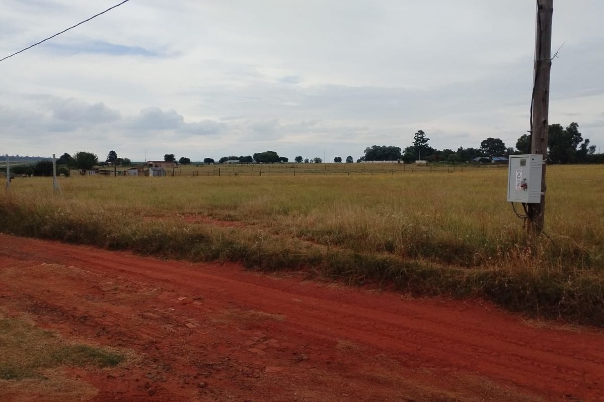 A view of the open land and perimeter fencing from the dirt road, featuring an electrical utility connection point.