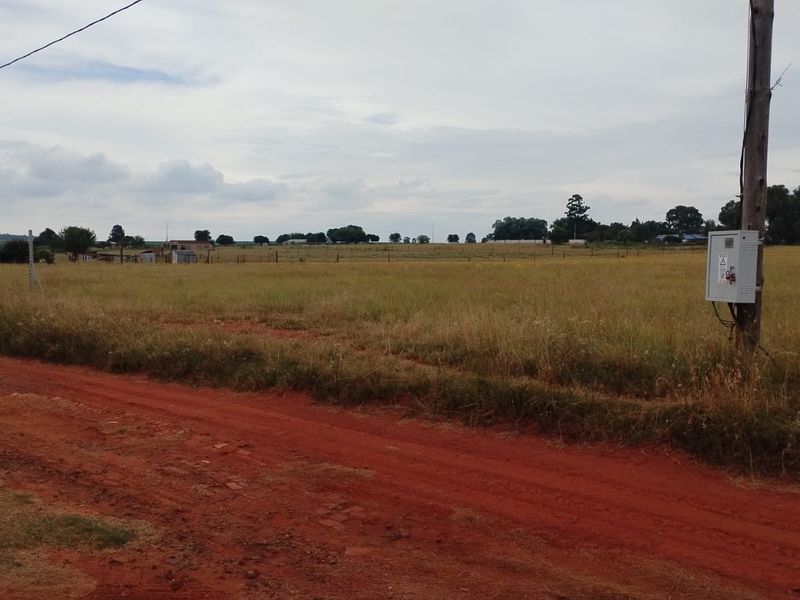 A view of the open land and perimeter fencing from the dirt road, featuring an electrical utility connection point.