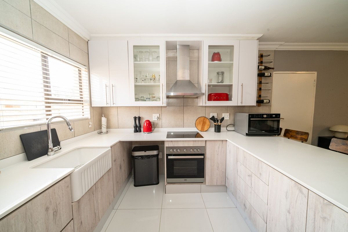 Modern kitchen featuring light wood-grain cabinetry, white quartz countertops, a farmhouse sink, and integrated stainless steel appliances including an oven and extractor fan.