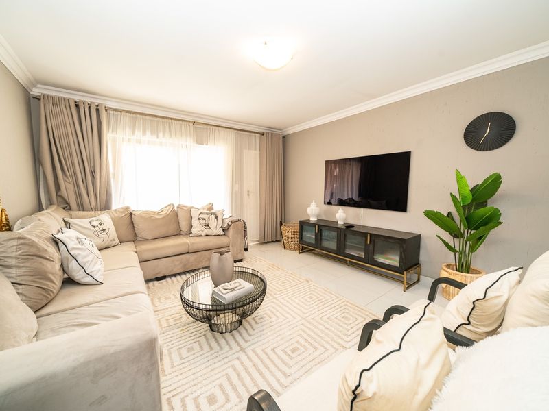 A well-maintained living room featuring neutral tiled flooring, cove cornicing, and large windows with curtain tracks, creating a bright and comfortable living space.