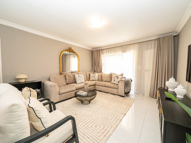 A bright and well-maintained living room featuring neutral wall tones, polished tiled flooring, and a large sliding glass door providing natural light.