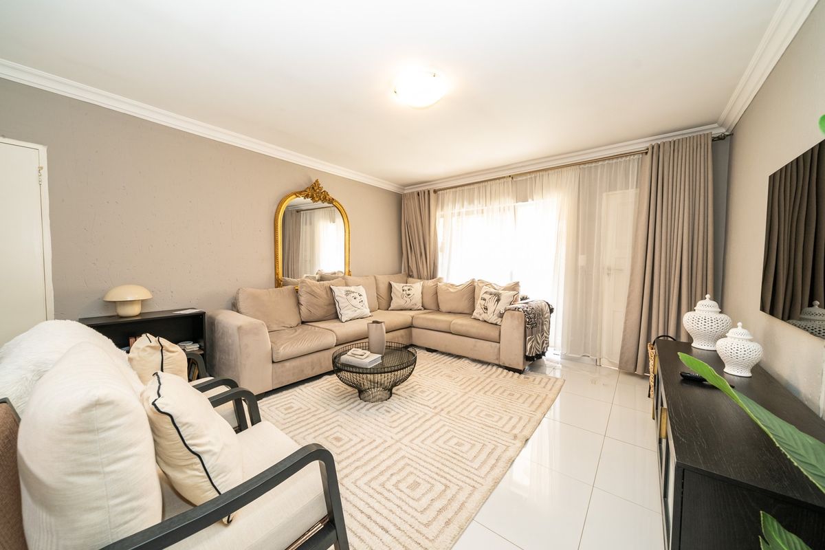 A bright and well-maintained living room featuring neutral wall tones, polished tiled flooring, and a large sliding glass door providing natural light.