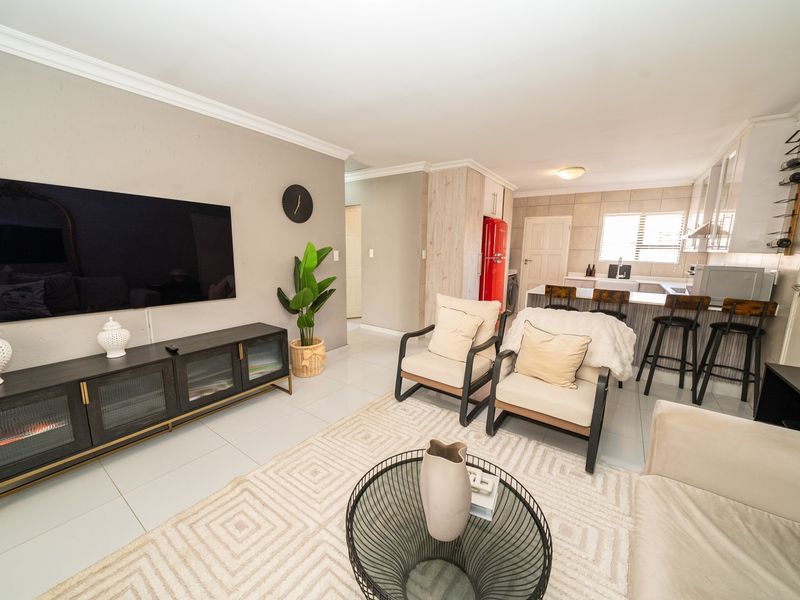 An open-plan living and kitchen area featuring tiled flooring, modern cabinetry, a breakfast island, and a bright, functional layout suitable for contemporary living.