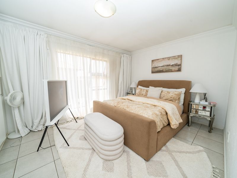 A well-maintained bedroom featuring neutral tiled flooring, built-in cupboards, and large windows with floor-to-ceiling curtains allowing for ample natural light.